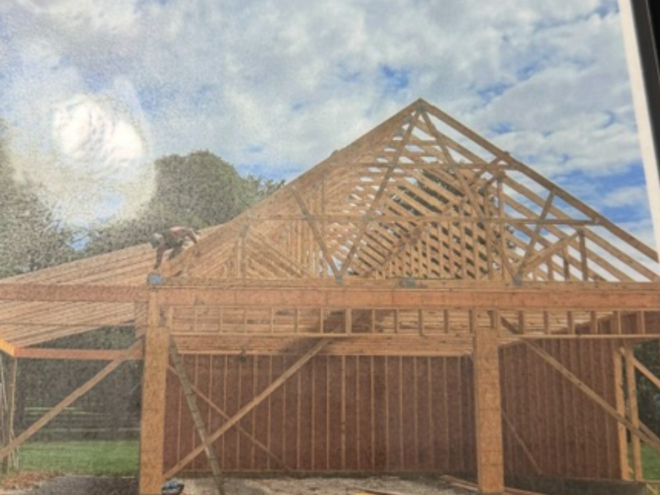 Wooden barn frame under construction with exposed roof trusses and framing against blue sky