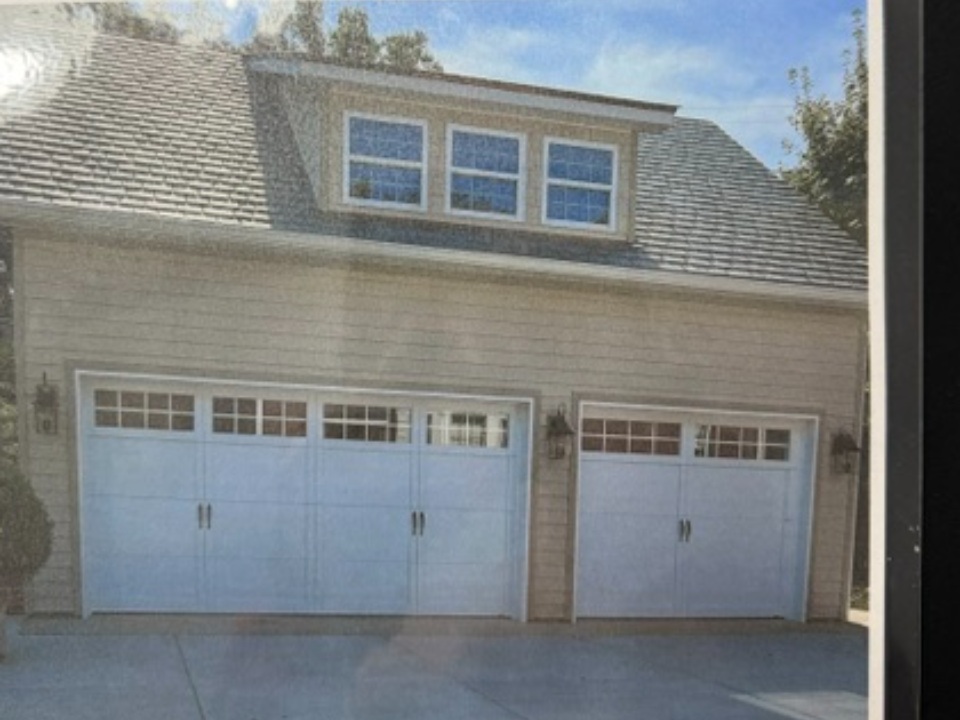 White garage doors on brick home with dormer windows